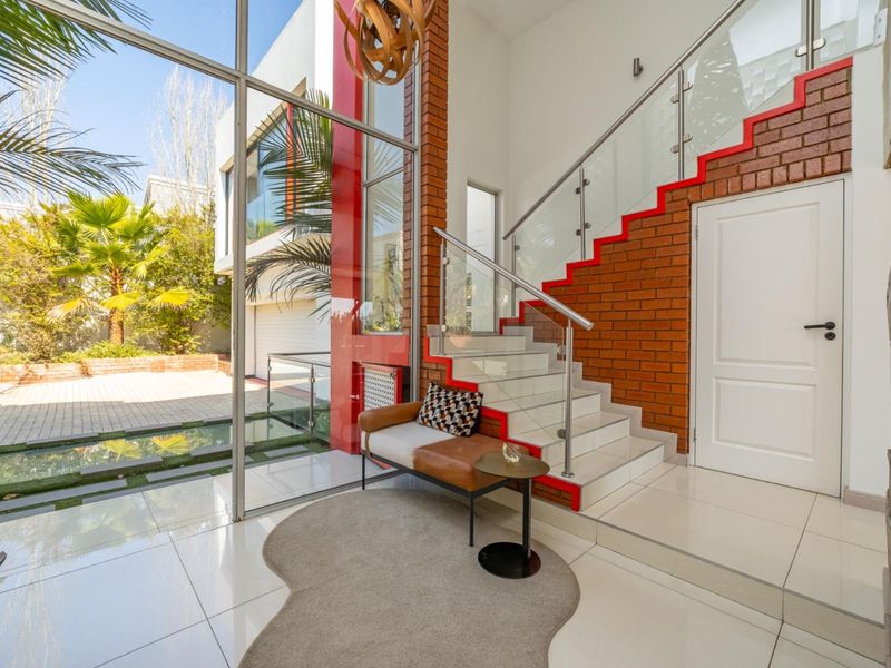Modern entrance hall featuring a striking glass staircase, exposed brick accents, and floor-to-ceiling windows overlooking the exterior courtyard.