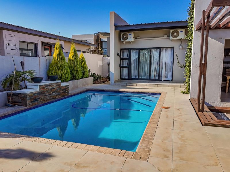 A well-maintained outdoor pool area featuring a tiled patio, stone-clad water feature, and direct access to the home via sliding glass doors.
