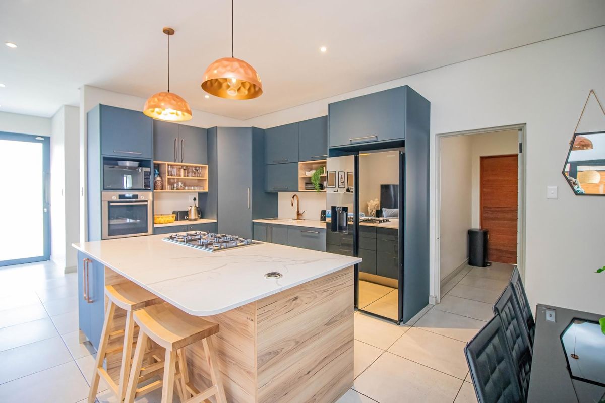 Modern kitchen featuring blue cabinetry, a central island with a gas hob, stone countertops, built-in appliances, and contemporary pendant lighting.