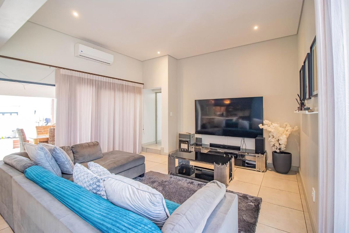 A bright and modern living room featuring tiled flooring, recessed downlighting, and a wall-mounted air conditioning unit, with direct access to an outdoor area.