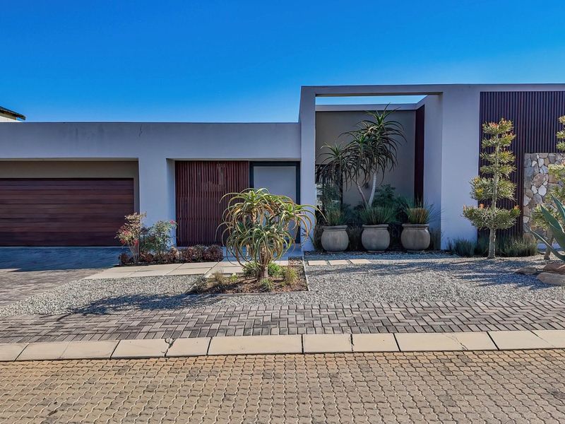 Modern front elevation featuring a timber garage door, stone cladding, and clean architectural lines with a paved driveway and landscaped entrance.