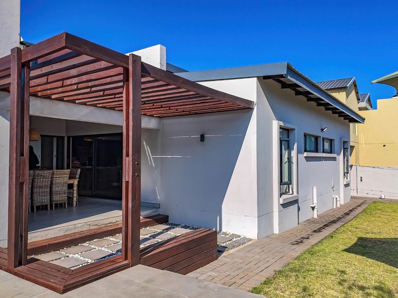 Rear view of the property featuring a timber pergola over a tiled patio, paved walkway, and a well-maintained lawn.