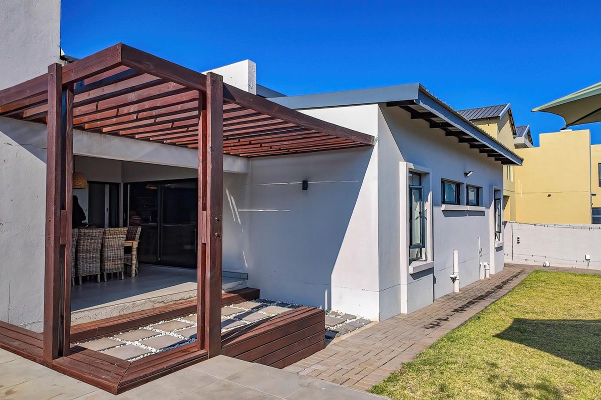 Rear view of the property featuring a timber pergola over a tiled patio, paved walkway, and a well-maintained lawn.