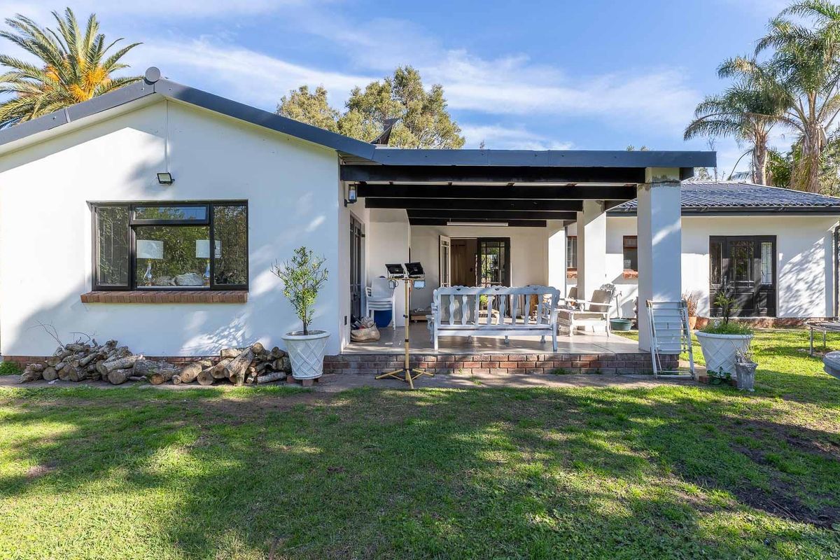 A well-maintained rear exterior view featuring a covered patio area, brick foundation, and established garden surroundings.