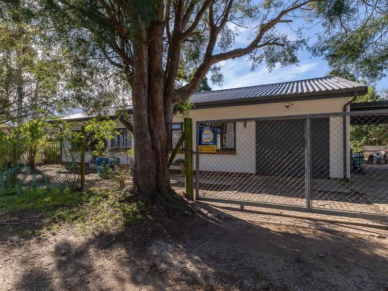 Front exterior view of the house featuring a gated driveway, carport, and established garden area.