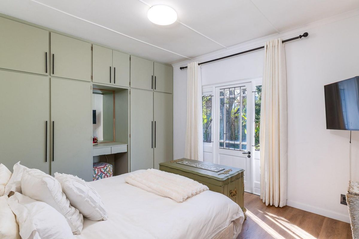 A well-maintained bedroom featuring extensive built-in cupboards with an integrated vanity, laminate flooring, and direct access to the garden through a secure door.