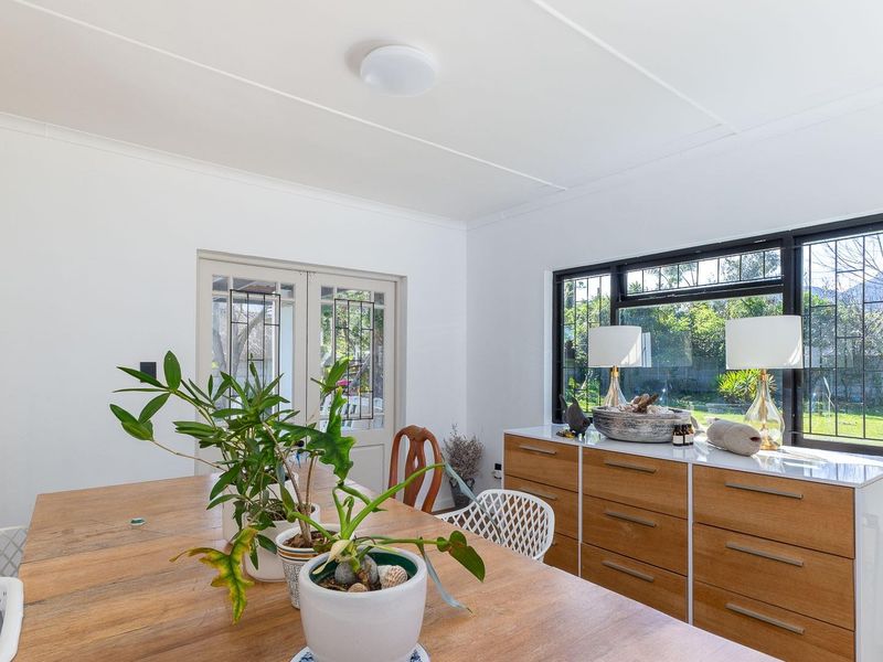 Bright dining area featuring large black-framed windows, neutral walls, and direct access to the garden through classic french doors.