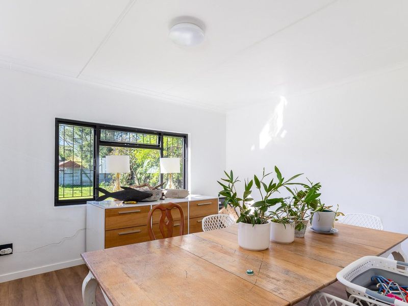 A bright dining room featuring laminate flooring, a large black-framed window with security bars, and a neutral white interior finish.