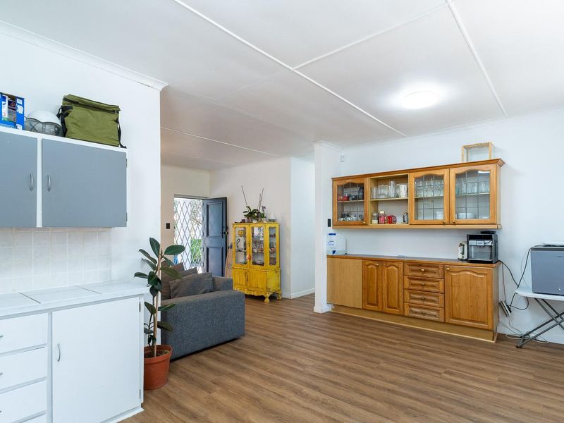 Open plan living area featuring laminate flooring and a combination of white and timber built-in cabinetry, providing versatile space for dining or storage.
