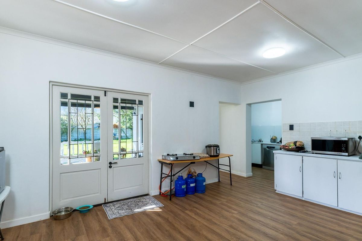 A functional kitchen area featuring laminate flooring, built-in cabinetry with tiled splashbacks, and double glass panel doors leading to the exterior.