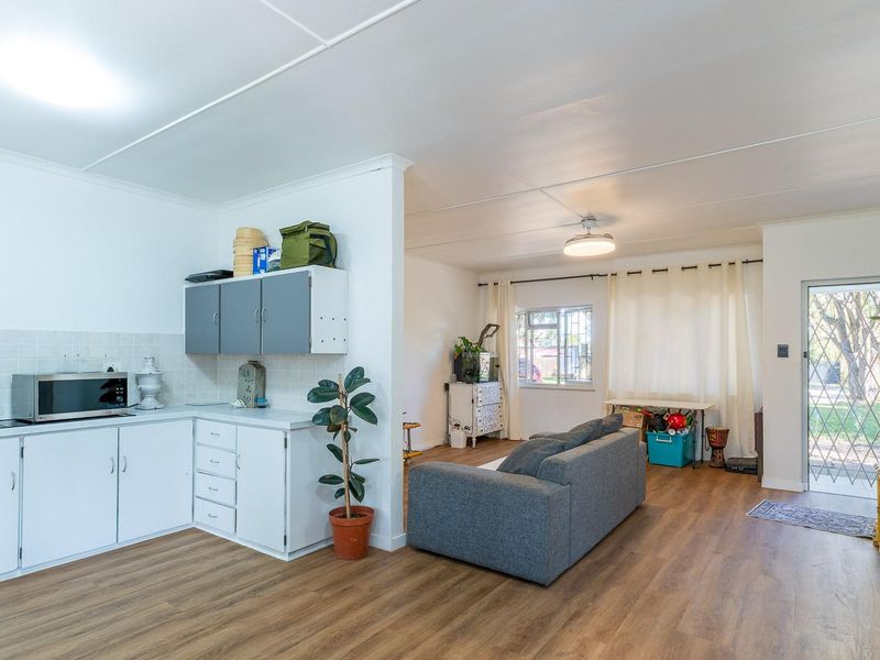 Open-plan living area featuring laminate flooring, a functional kitchen with built-in cabinetry, and direct access to the exterior through a security gate.