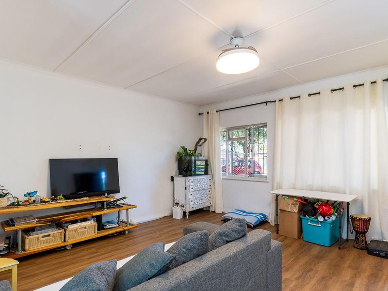 A bright living room featuring laminate flooring, a ceiling fan, and large windows with curtain rods, offering a functional and neutral living space.