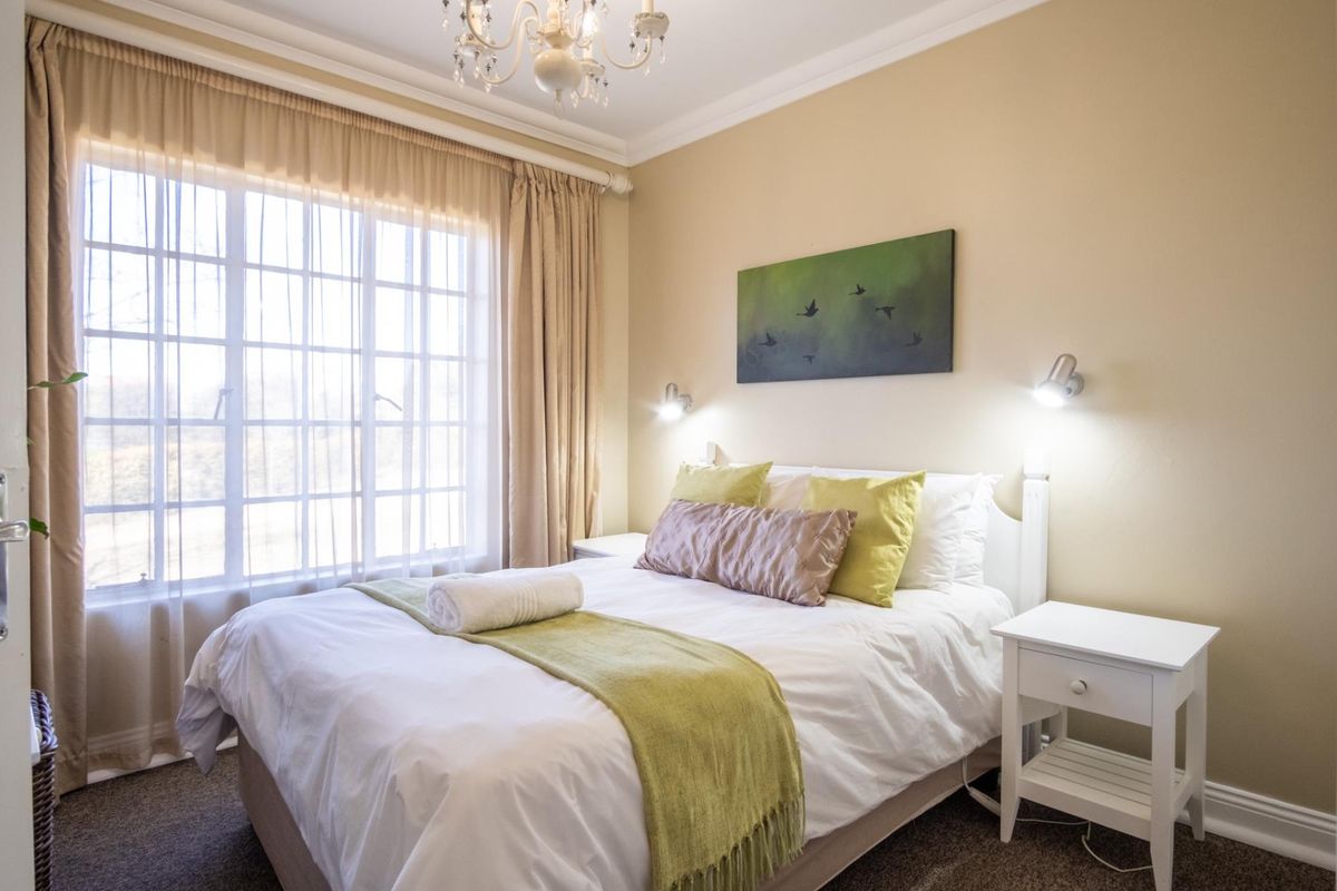 A well-maintained bedroom featuring crown molding, wall-mounted reading lights, and a large window allowing for natural light.