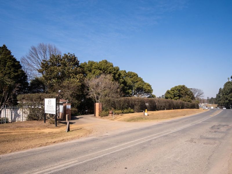 Street view of the property entrance featuring perimeter fencing, a brick pillar, and signage along a paved road.