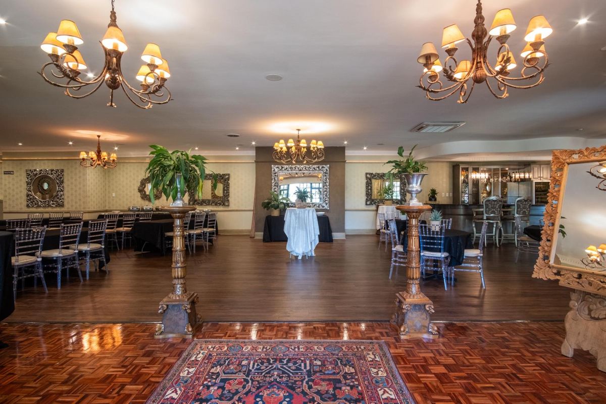 Spacious event hall featuring elegant chandeliers, a combination of parquet and laminate flooring, and a built-in bar area, suitable for formal gatherings.