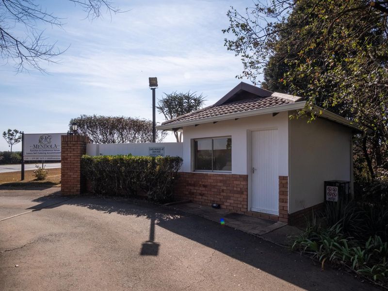 A well-maintained security guard house at the property entrance, featuring brick accents, a tiled roof, and a paved driveway approach.