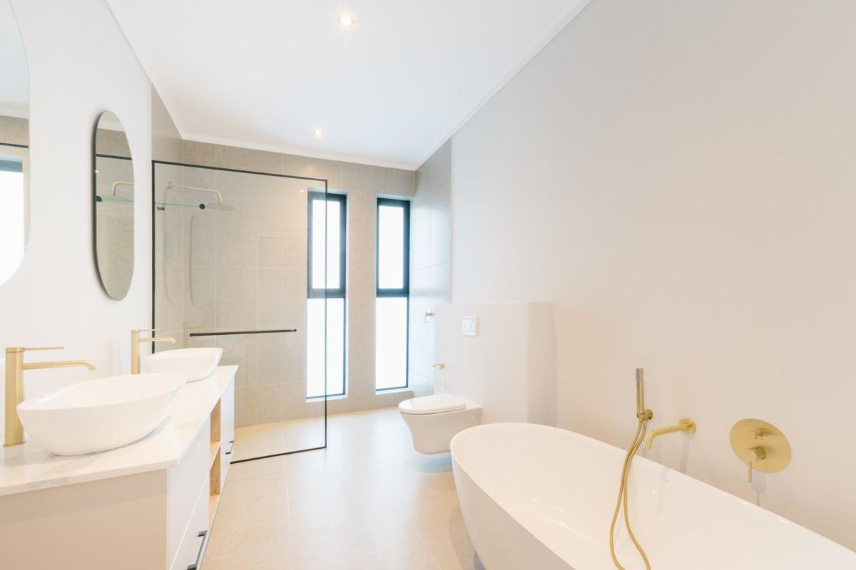 Modern, high-end bathroom featuring a double vanity, freestanding bathtub, walk-in shower with glass screen, and wall-hung toilet with contemporary brass fixtures.