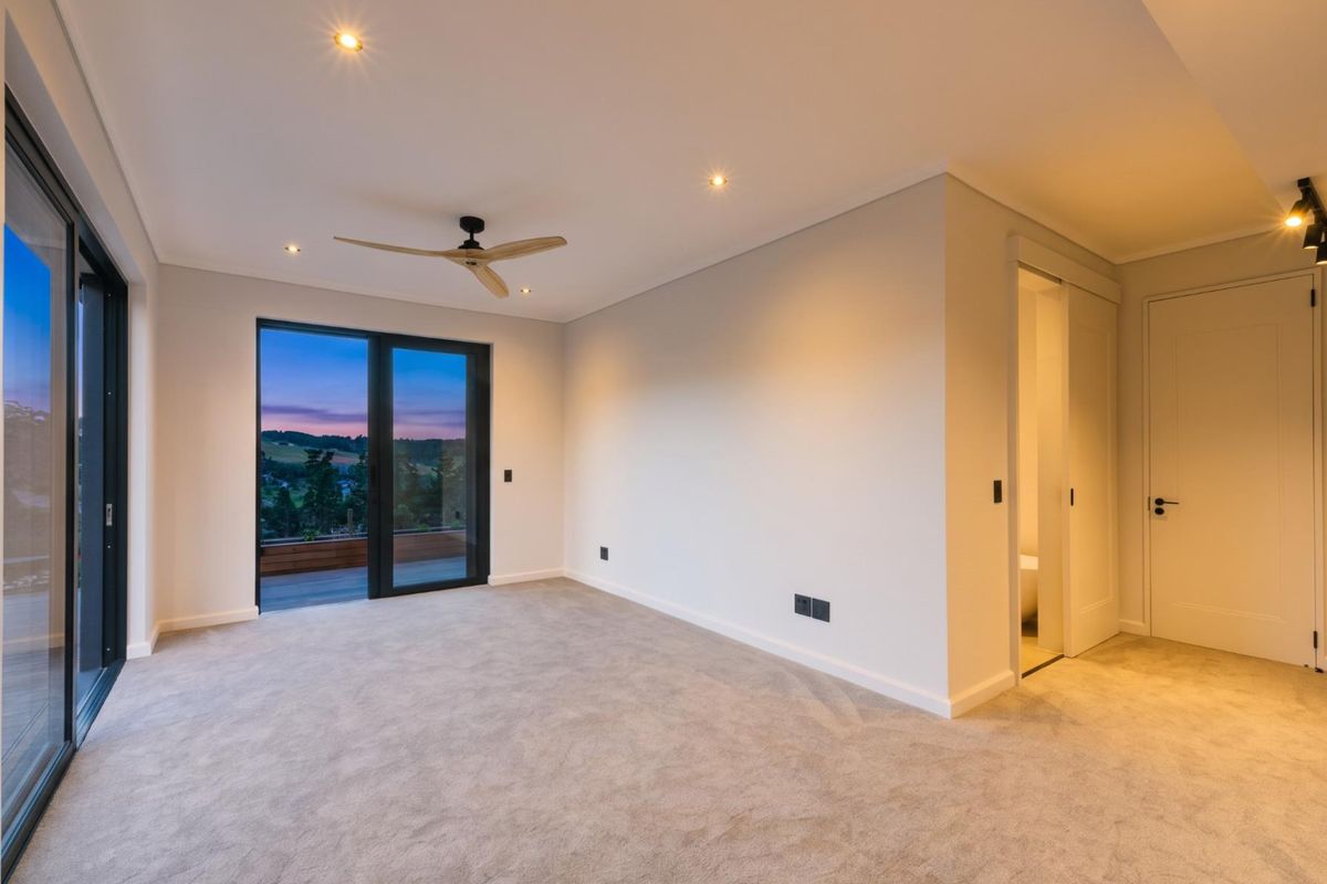 A spacious, modern bedroom featuring neutral carpeting, recessed lighting, a ceiling fan, and large sliding glass doors leading to an outdoor area.
