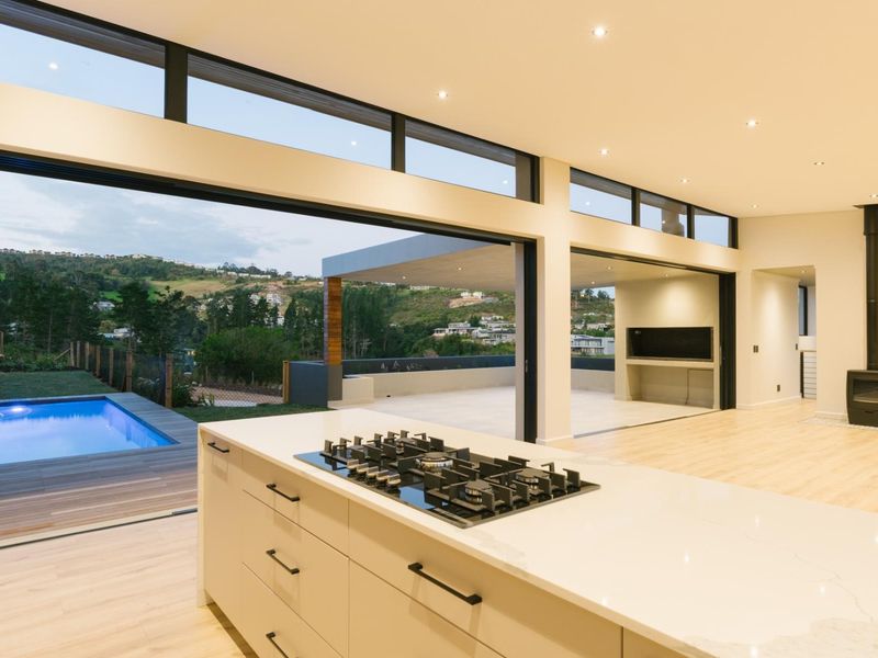 Modern open-plan living area featuring a sleek kitchen island with gas cooktop, seamless indoor-outdoor flow to a covered patio and swimming pool.