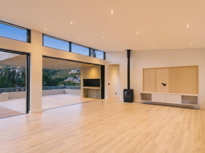 Spacious, modern living area featuring light laminate flooring, a wood-burning fireplace, built-in cabinetry, and large sliding doors opening to a scenic outdoor patio.