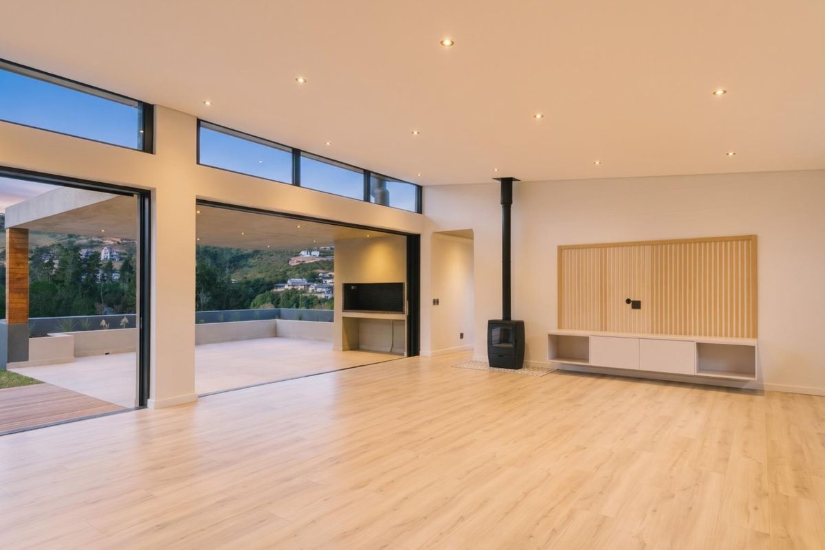 Spacious, modern living area featuring light laminate flooring, a wood-burning fireplace, built-in cabinetry, and large sliding doors opening to a scenic outdoor patio.