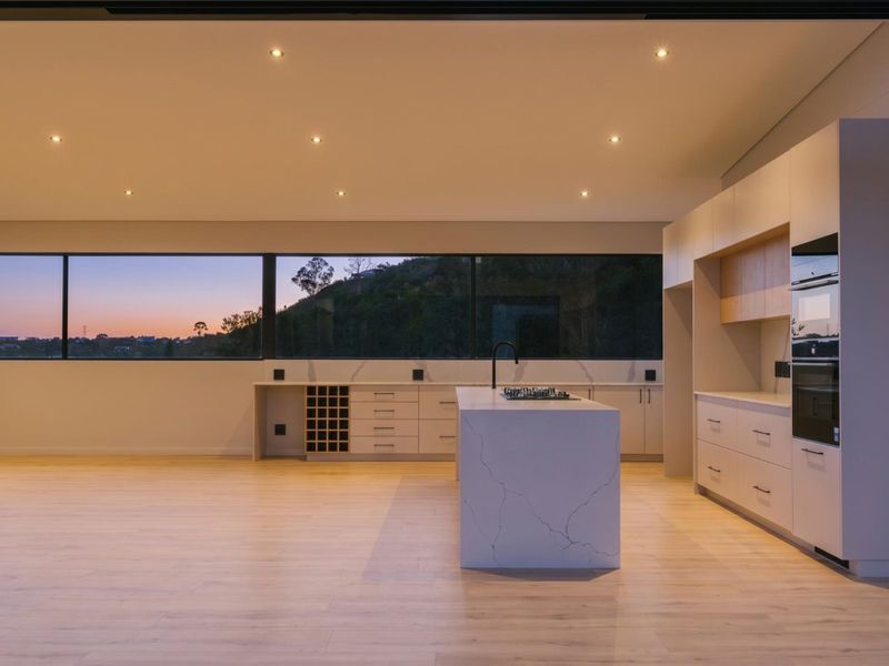 Modern, minimalist kitchen featuring a large stone island, integrated cabinetry, built-in appliances, and expansive windows with scenic views.