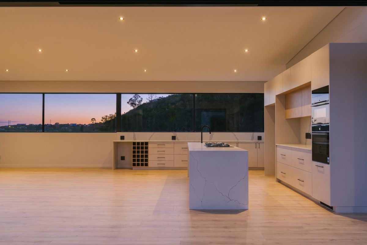 Modern, minimalist kitchen featuring a large stone island, integrated cabinetry, built-in appliances, and expansive windows with scenic views.