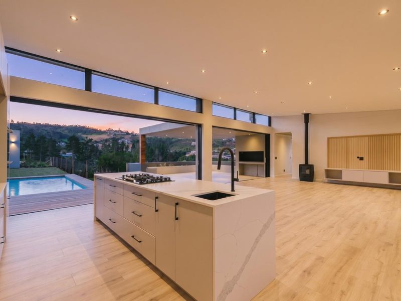 Spacious open-plan living area featuring a modern kitchen island, sleek cabinetry, wood-burning fireplace, and seamless indoor-outdoor flow to a pool deck with scenic views.