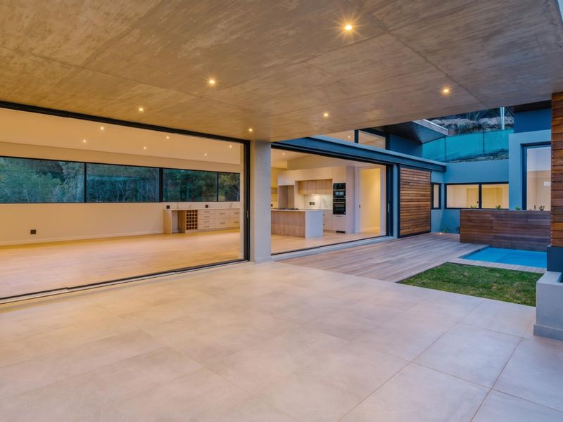 Modern open-plan living area seamlessly connecting to a covered patio, wooden deck, and swimming pool through large sliding glass doors.
