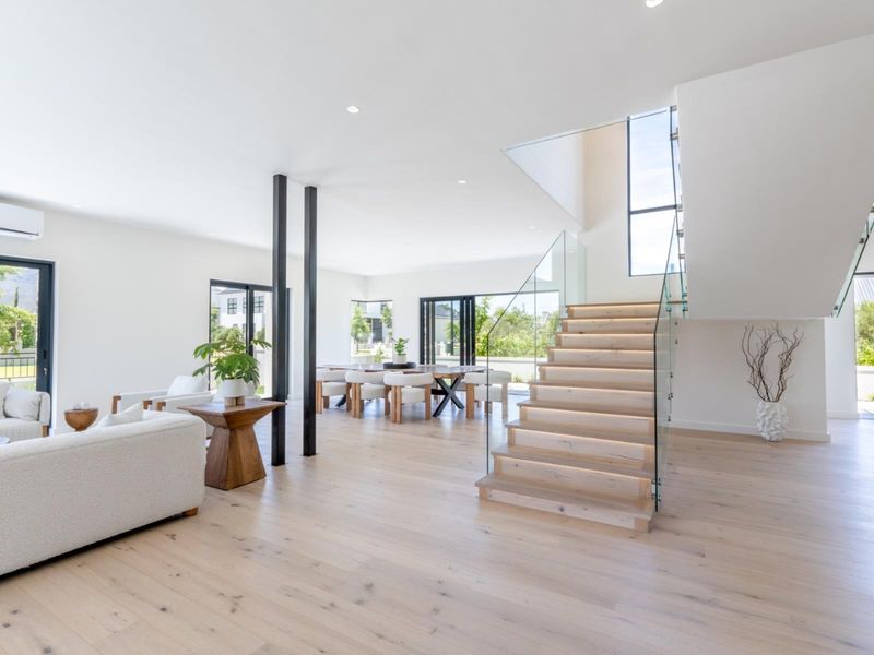 Spacious open-plan living and dining area featuring light timber flooring, a modern staircase with glass balustrades, and seamless access to the outdoors.