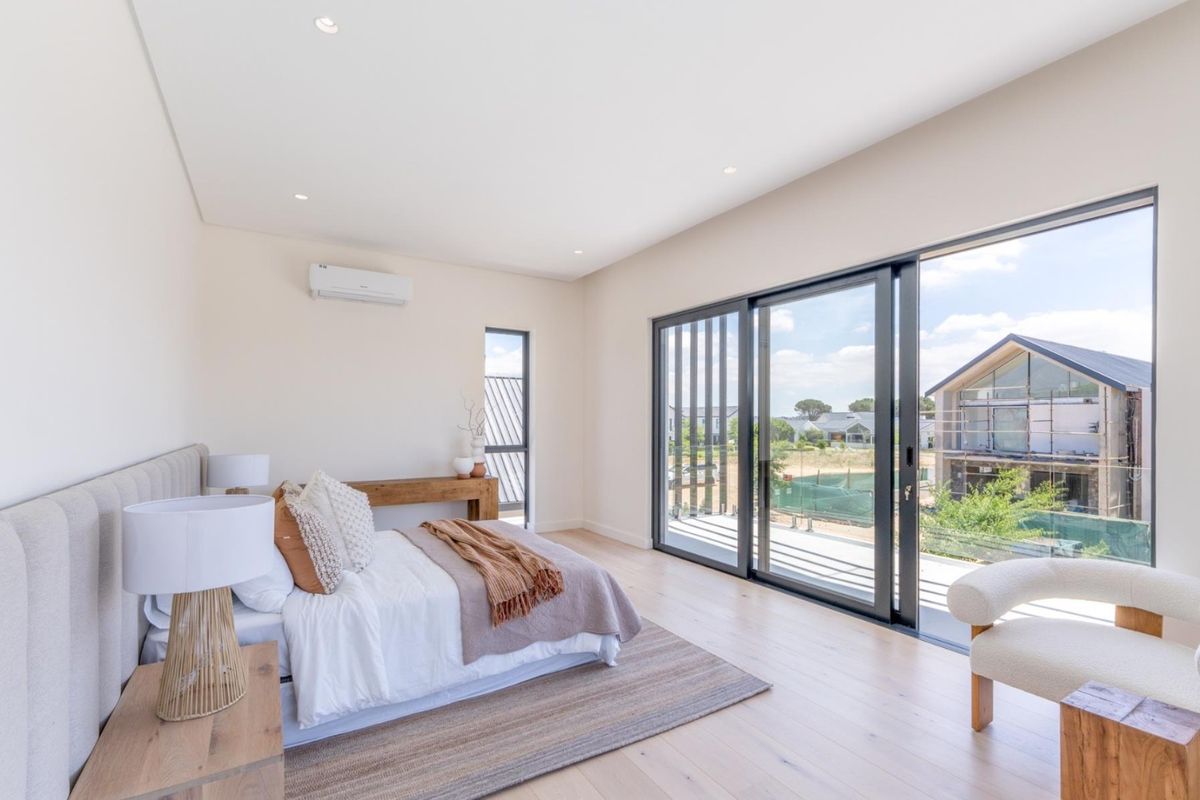 Modern, light-filled bedroom featuring timber flooring, recessed lighting, and large sliding glass doors opening onto a private balcony with scenic views.