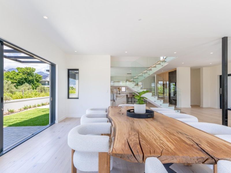 Spacious open-plan living area featuring modern timber flooring, a glass balustrade staircase, and large sliding doors opening to the garden.
