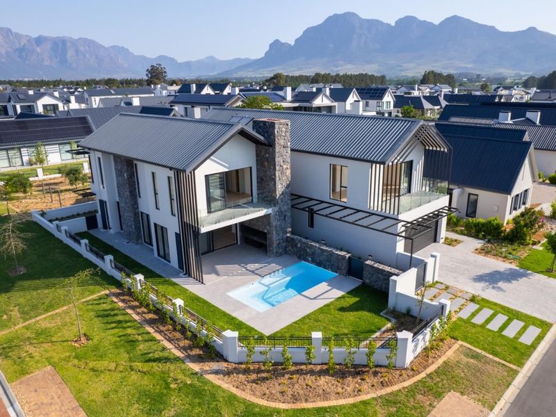 Aerial view of a modern two-story residence featuring a swimming pool, stone-clad exterior, metal roofing, and a landscaped garden in a residential estate.