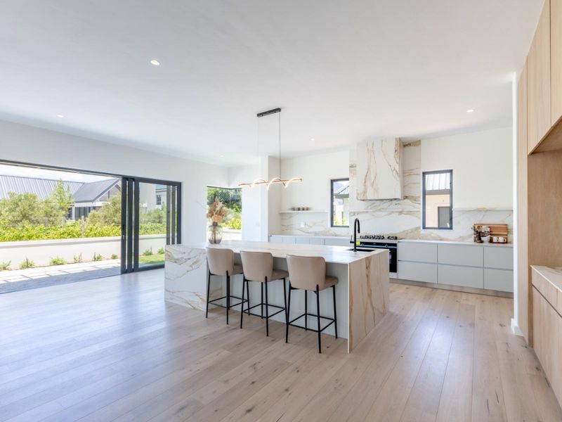 Modern open-plan kitchen featuring a marble island, premium cabinetry, and seamless flow to the outdoor patio through large sliding glass doors.