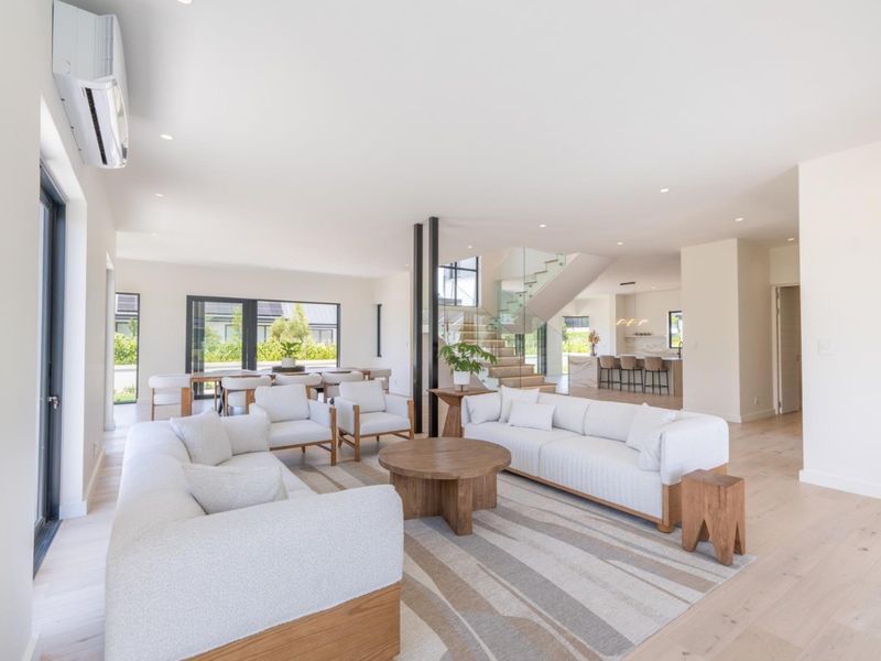Spacious open-plan living area featuring light timber flooring, a modern staircase with glass balustrades, and seamless flow to the kitchen and dining space.
