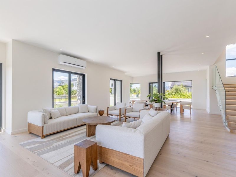Spacious open-plan living and dining area featuring light timber flooring, recessed lighting, modern aluminium windows, and a contemporary staircase with glass balustrades.
