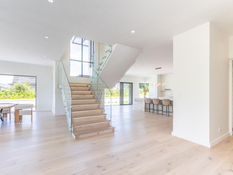 Spacious open-plan living area featuring a modern timber staircase with glass balustrades, light timber flooring, and a sleek kitchen with a stone island.