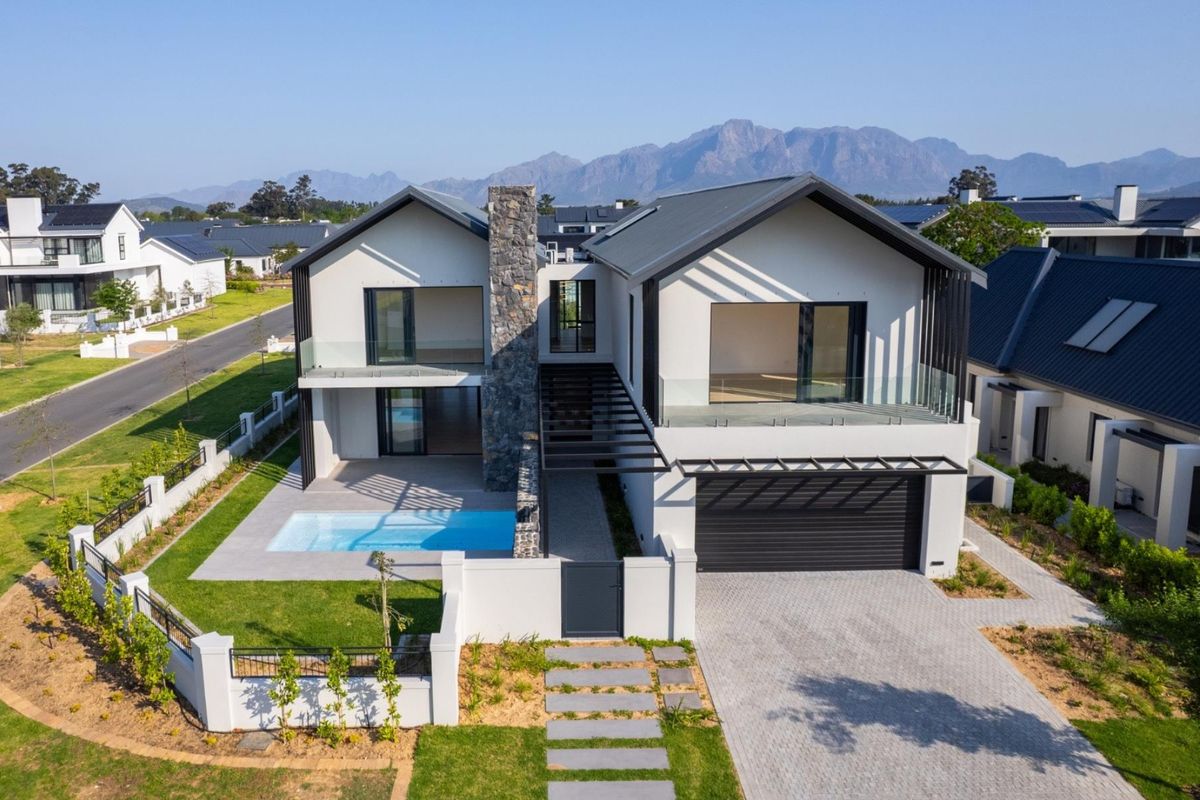 Aerial view of a modern two-story residence featuring a swimming pool, stone chimney, paved driveway, and mountain views in a secure estate.