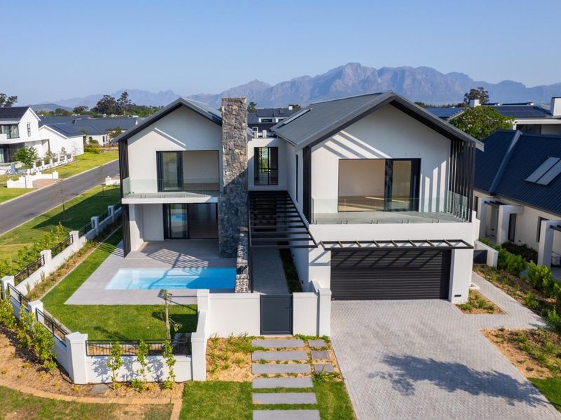 Aerial view of a modern two-story residence featuring a swimming pool, stone chimney, paved driveway, and mountain views in a secure estate.