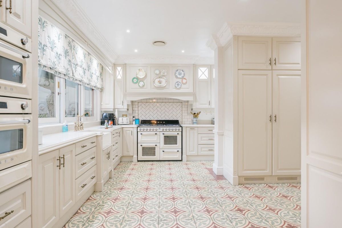 A bright, well-appointed kitchen featuring classic cabinetry, a farmhouse sink, a range cooker, and decorative patterned floor tiles.