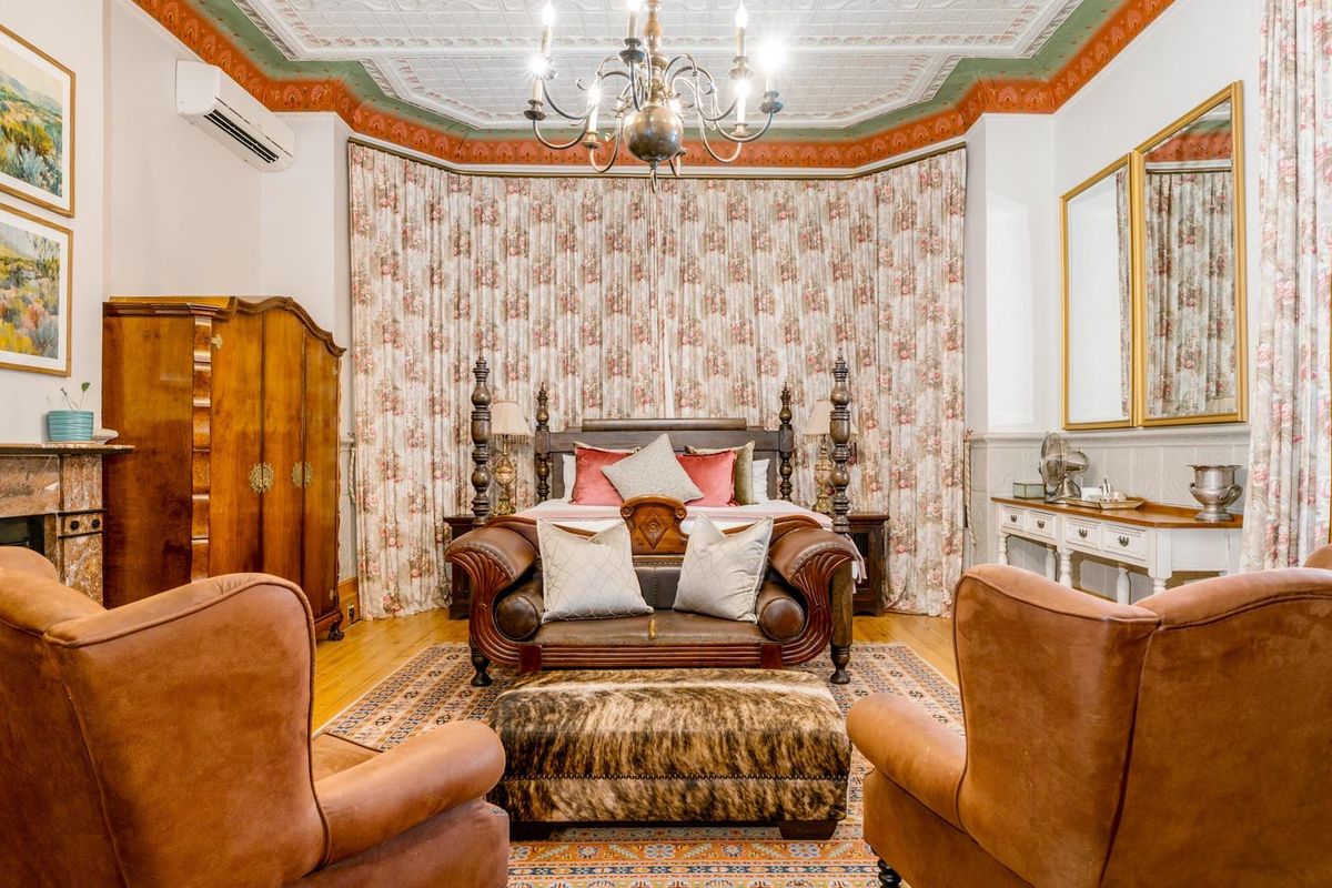 Spacious bedroom featuring an ornate pressed metal ceiling, timber flooring, and a classic fireplace with a marble mantel.