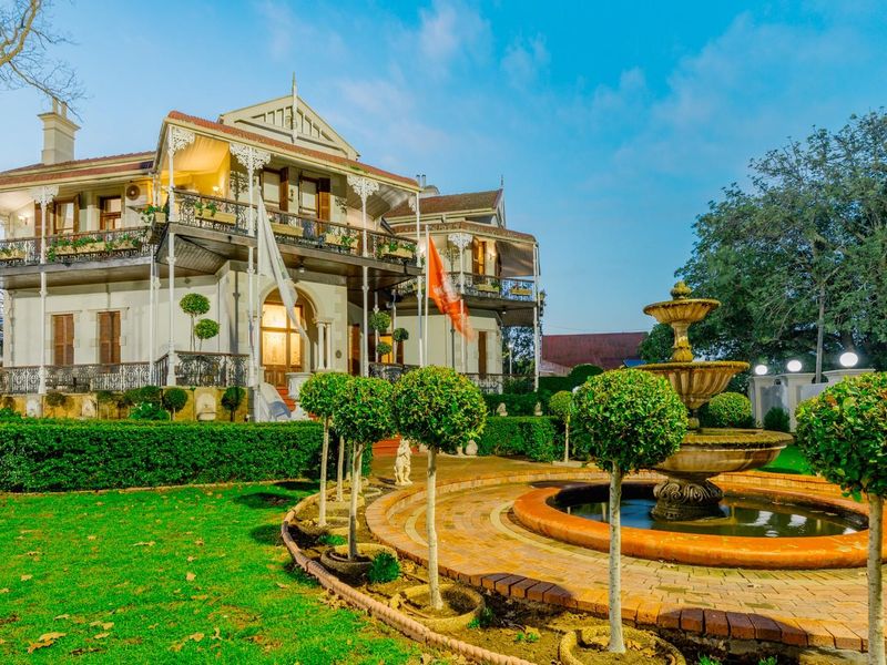 A grand historic residence featuring a multi-level wrought iron balcony, an ornamental fountain, and meticulously landscaped gardens.