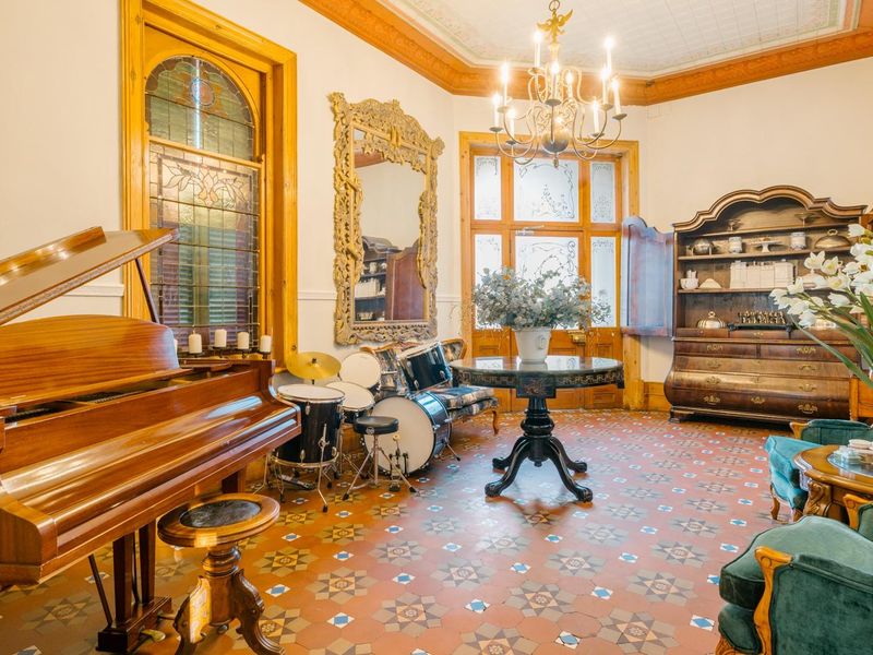 Elegant living room featuring original patterned encaustic floor tiles, ornate timber door frames, stained glass windows, and a decorative ceiling with a classic chandelier.