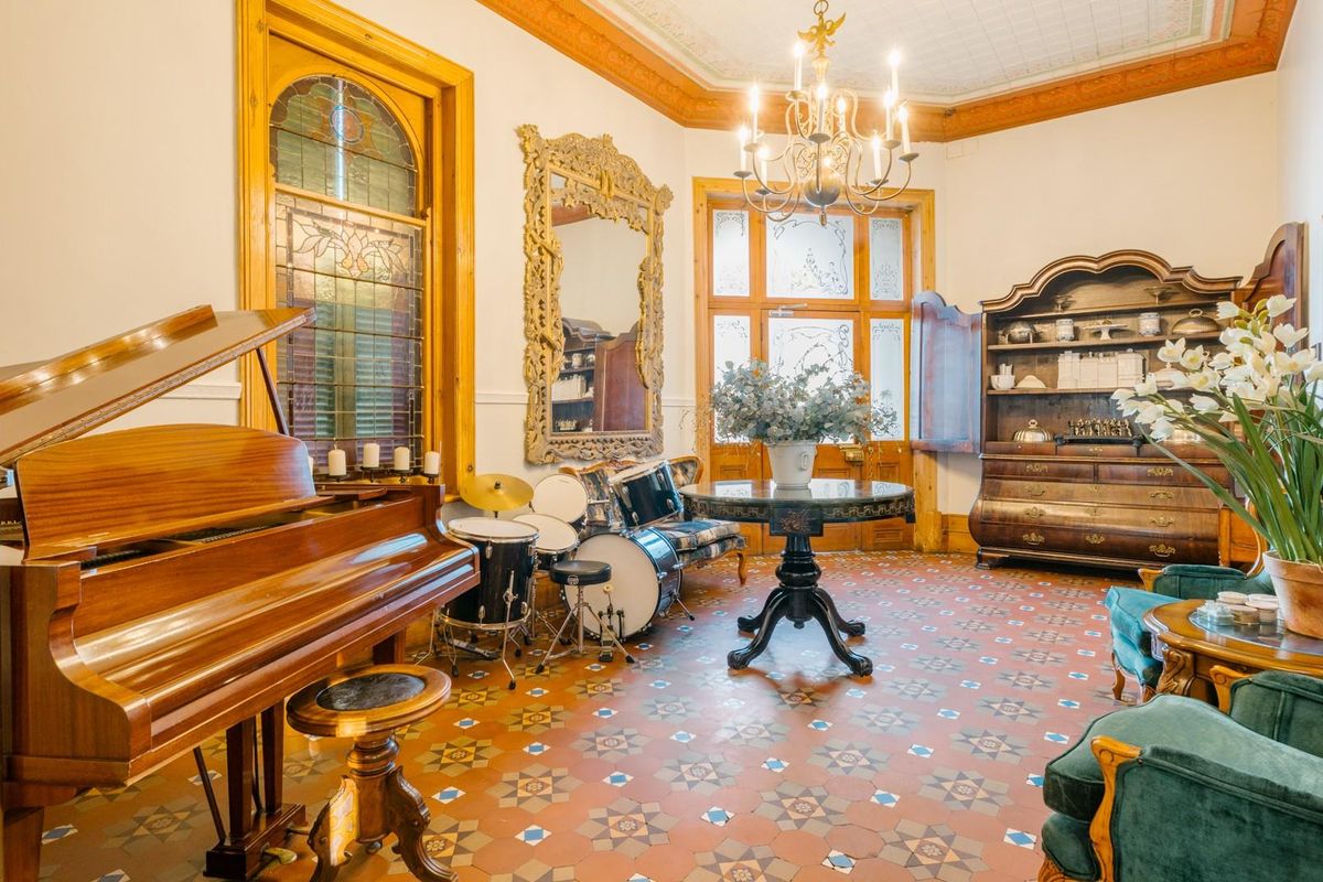 Elegant living room featuring original patterned encaustic floor tiles, ornate timber door frames, stained glass windows, and a decorative ceiling with a classic chandelier.