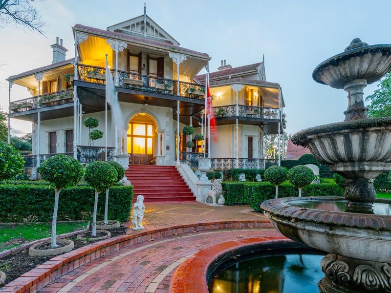 Grand historic residence featuring a multi-level veranda, intricate wrought iron detailing, and a beautifully landscaped front garden with a central stone fountain.