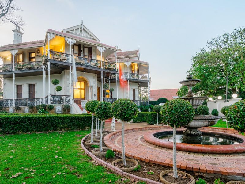 A grand historic residence featuring an ornate wrought iron balcony, a classic stone fountain, and meticulously landscaped gardens.