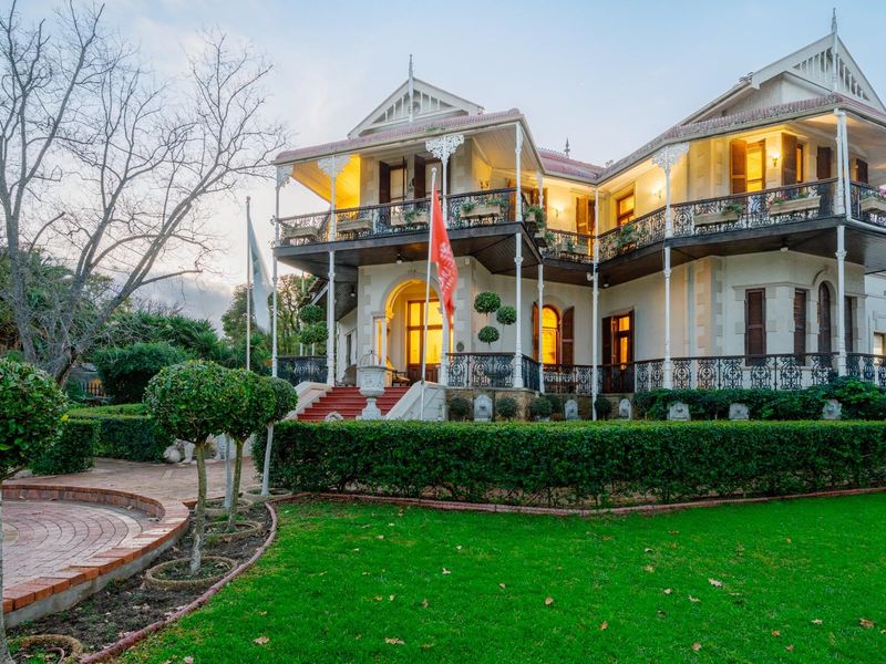 A grand, well-maintained historic residence featuring a two-story veranda with intricate wrought iron detailing, set within a beautifully landscaped garden.