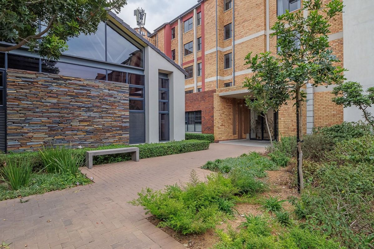 A well-maintained exterior courtyard area featuring stone cladding, brick building facades, and a paved walkway surrounded by landscaped garden beds.