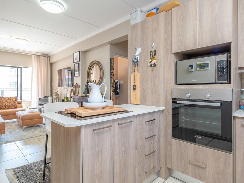 Open-plan living area featuring a modern kitchen with wood-finish cabinetry, integrated appliances, and seamless flow to the adjacent lounge and balcony.