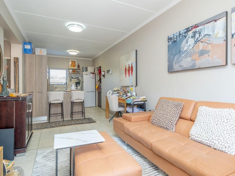 Open-plan living area featuring a compact kitchen with built-in cabinetry and tiled flooring, seamlessly integrated with the lounge space.